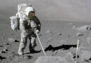 An astronaut in a white spacesuit stands on the surface of the moon with a metal detector.