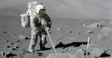 An astronaut in a white spacesuit stands on the surface of the moon with a metal detector.