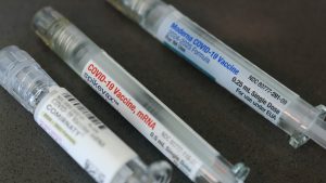 Three labeled COVID-19 vaccine syringes lie on a dark surface.