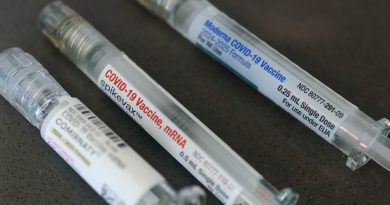Three labeled COVID-19 vaccine syringes lie on a dark surface.
