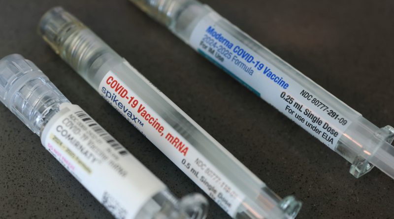 Three labeled COVID-19 vaccine syringes lie on a dark surface.