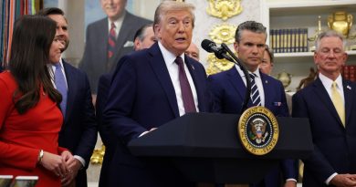 people in suits stand behind a microphone at a lectern in a richly decorated office