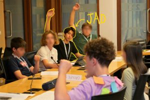 Photo d'ados à une table officielle du CESE avec micros intégrés. Certains lèvent la main pour prendre la parole. C'est le cas de Jad