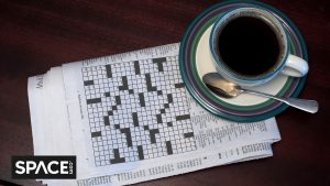 A black and white crossword puzzle sits underneath a blue and white coffee cup with the Space.com black and white logo in the bottom left corner.