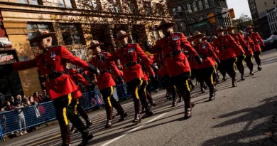 Des agents de la GRC en tenue rouge marchent en rang au milieu de la rue, devant un public qui les regarde.