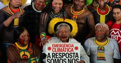 Le chef Raoni tenant une pancarte et entouré de plusieurs personnes autochtones.