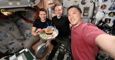 a man in a red shirt takes a selfie with two women in dark colored shirts as they hold up a makeshift cake with a &quot;200 Days&quot; embroidered patch mounted atop it.