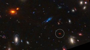 A deep space image showing the various colors of different galaxies, some red some white against a dark background