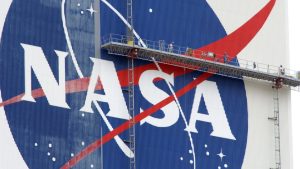 workers on scaffolding paint a nasa logo on a massive white building
