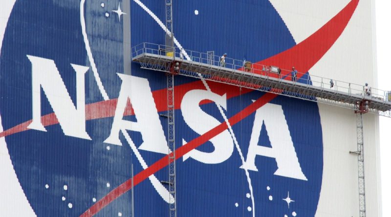 workers on scaffolding paint a nasa logo on a massive white building