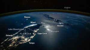 A photograph of the tip of Florida and nearby Cuba from space, with lights from cities illuminating the surface of the planet, labeled cities like Orlando and Tampa are seen as well as a green surface over Earth's labeled airglow