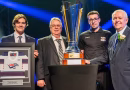 Quatre hommes posent avec un gros trophée et une plaque honorifique.