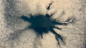 A dendritic shaped dark spot is seen against an icy surface
