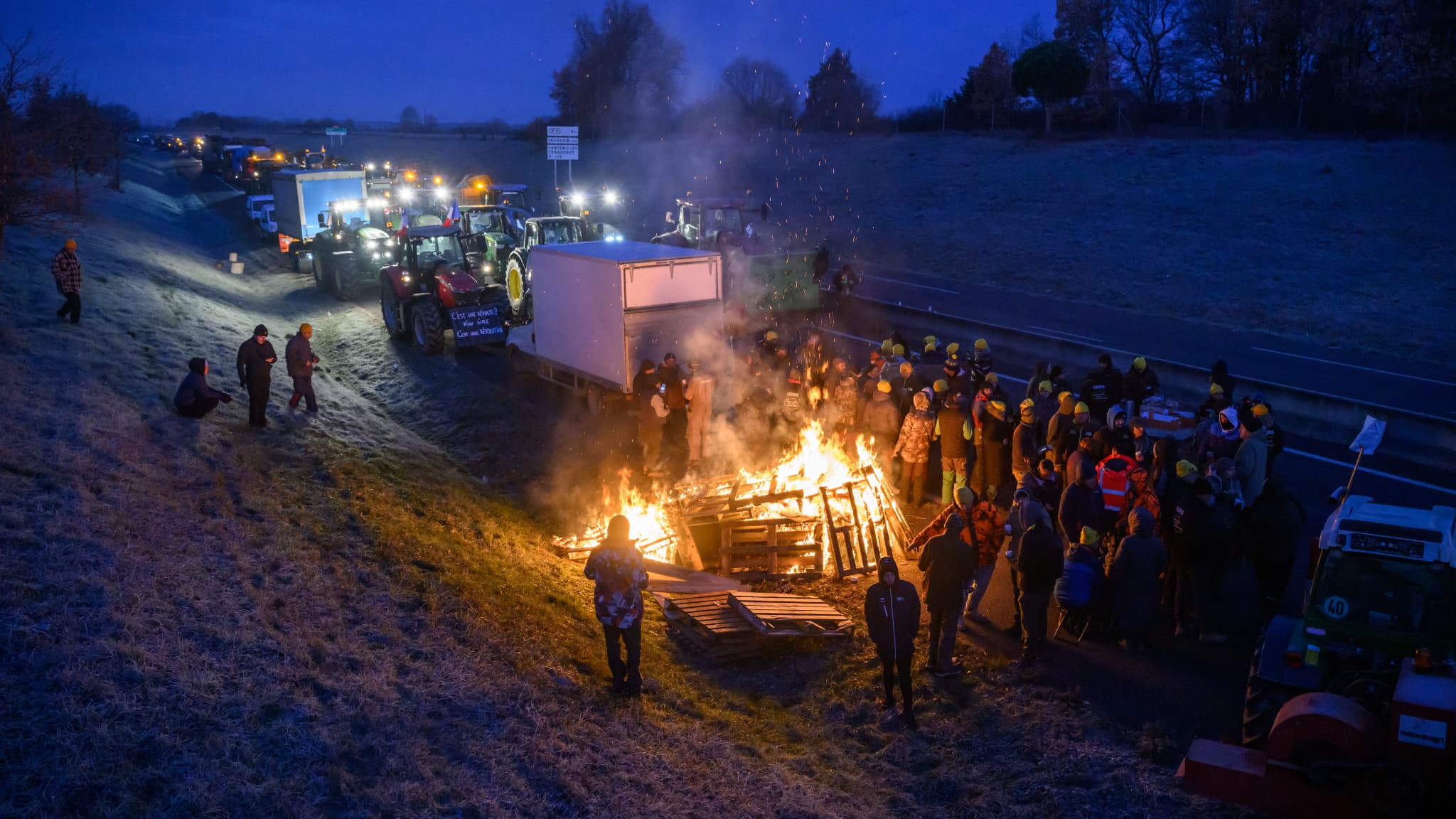 Des agriculteurs se réchauffent autour d'un feu alors qu'ils sont empêchés par les gendarmes d'entrer dans Toulouse dans le cadre de leur manifestation le 7 janvier 2026.