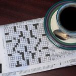A black and white crossword puzzle sits underneath a blue and white coffee cup with the Space.com black and white logo in the bottom left corner.