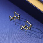 Une paire de boucles d'oreilles géométriques dorées conçues pour la mode street photography transfrontalière, émettant une impression de luxe