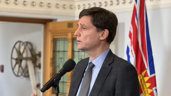 Un homme parle au micro. Derrière lui, le drapeau de la Colombie-Britannique.