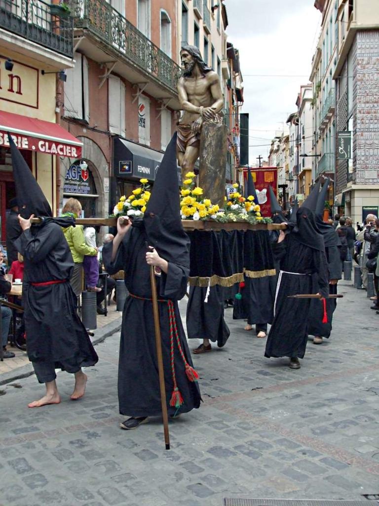 Des pénitents de la procession de la Sanch défilent dans les rues de Perpignan lors du Vendredi saint, portant une statue du Christ au cœur du centre historique.