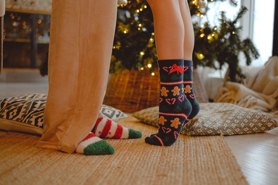 Close-up of couple's festive socks standing on a cozy carpet beside a Christmas tree.
