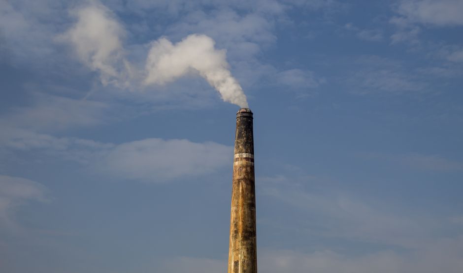 A factory chimney releasing smoke against a clear blue sky, highlighting air pollution.