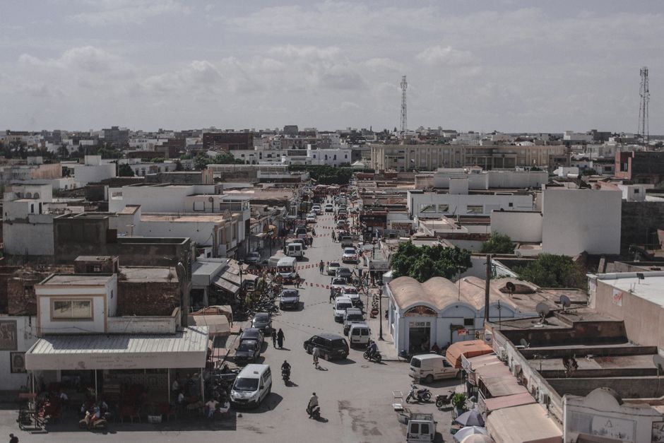 A bustling urban street in a town with cars and buildings, captured from above.