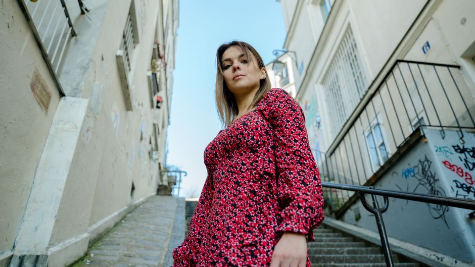 Stylish woman in a floral dress posing on urban steps in Paris, France.