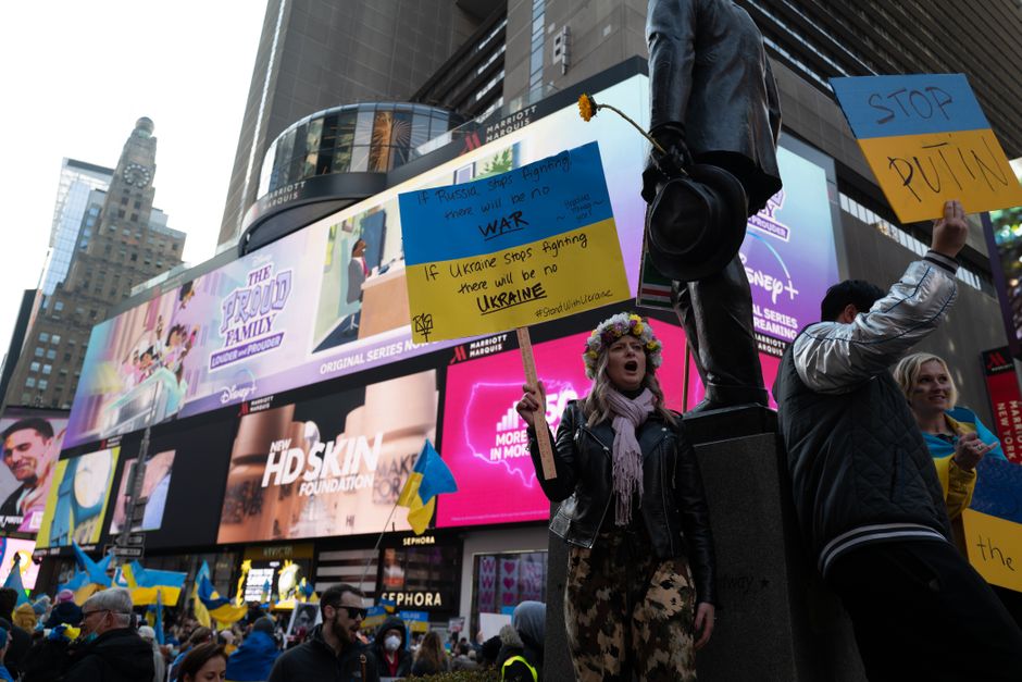 Protesters in Times Square holding anti-war signs and Ukrainian flags.