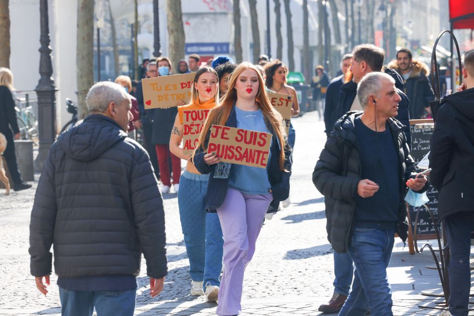 Women protesting in a city street holding signs in French, advocating for empowerment.