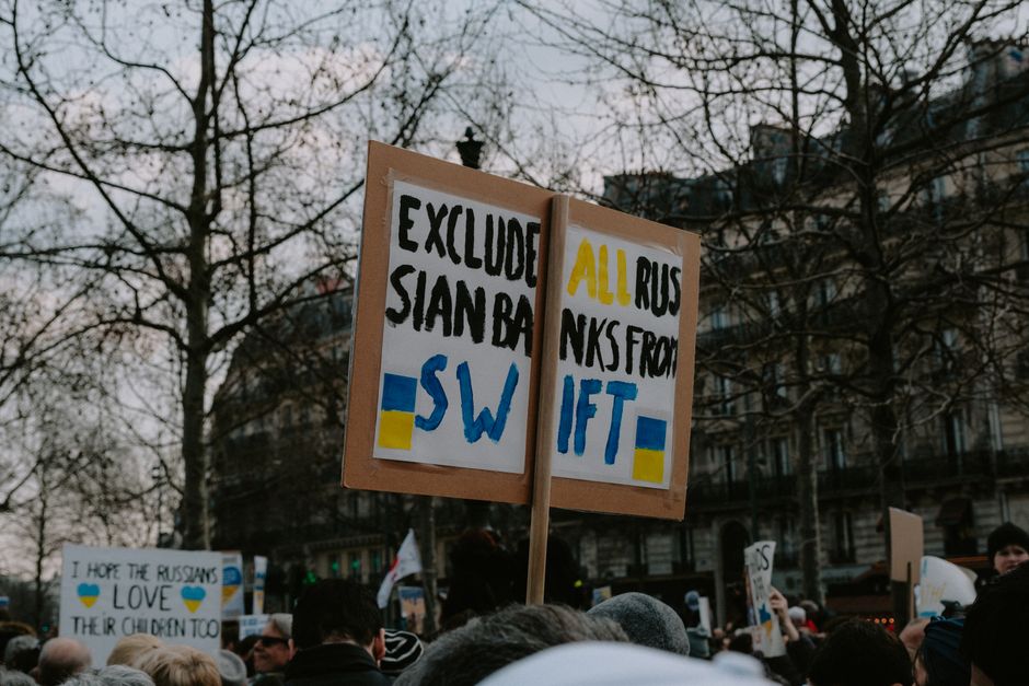 Crowd gathered with placards during a protest against Russian banks in an urban setting.