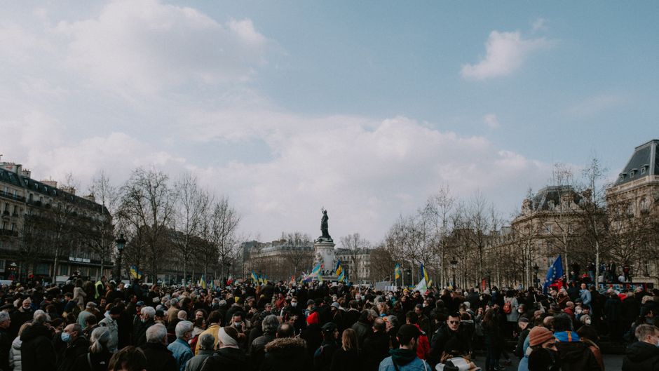 Protesters gather in a city square around a prominent monument.