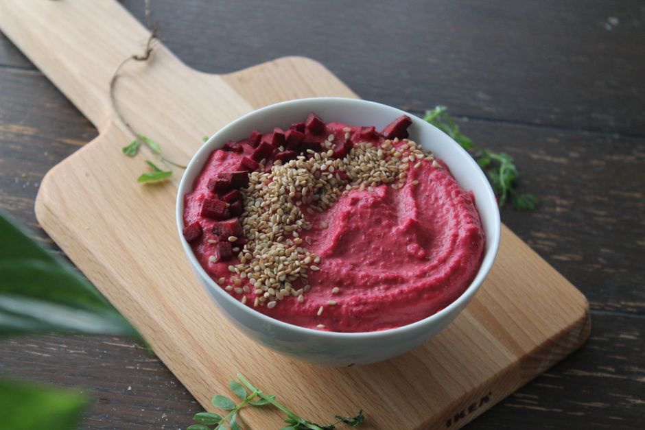 Colorful beetroot hummus garnished with sesame seeds in a white bowl on a wooden board.