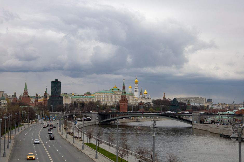 A scenic view of Moscow featuring the Kremlin, river, road, and cloudy sky.