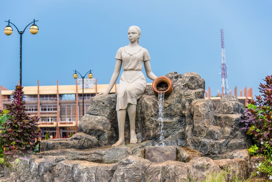 Sculpture of woman with flowing water in Yaoundé city center, vibrant outdoor setting.