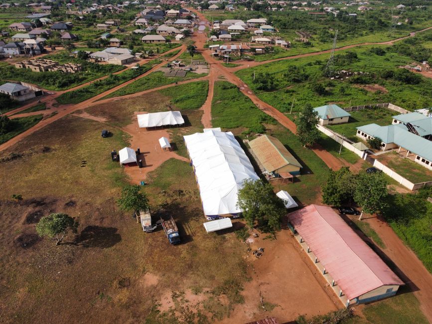 Drone shot of a rural area with tents and buildings amidst greenery.