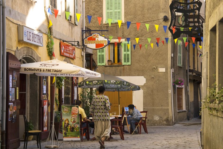 Colorful European street scene with quaint cafe and people relaxing outdoors.