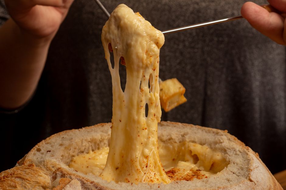 Mouthwatering close-up of gooey melted cheese fondue being stretched from a bread bowl.