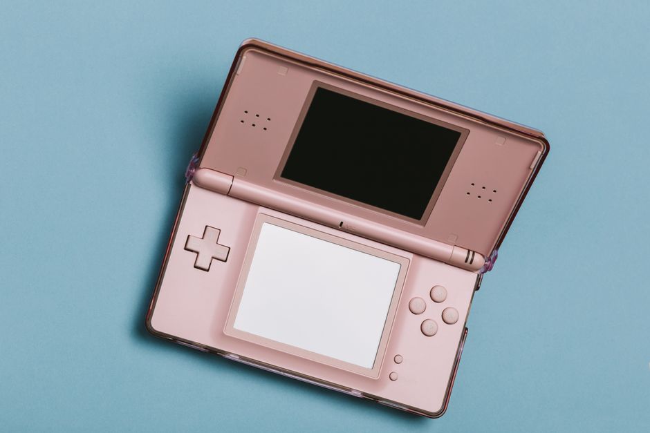 Close-up of a pink portable gaming console with dual screens on a blue surface.