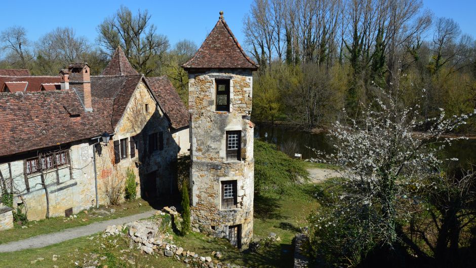 Charming rustic stone building with tower surrounded by lush trees during springtime.