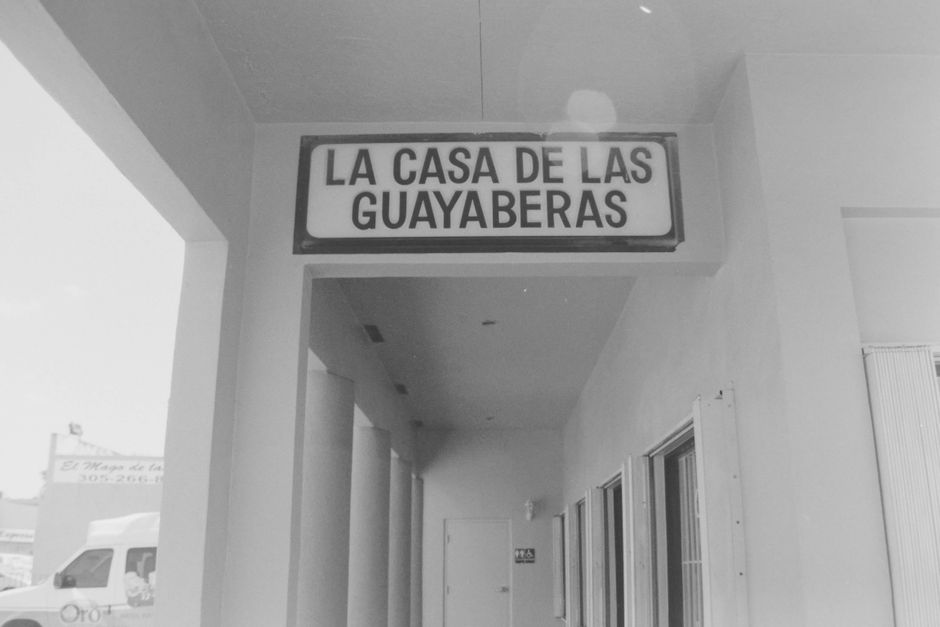 Black and white image of a clothing store corridor with sign 'La Casa de las Guayaberas'.