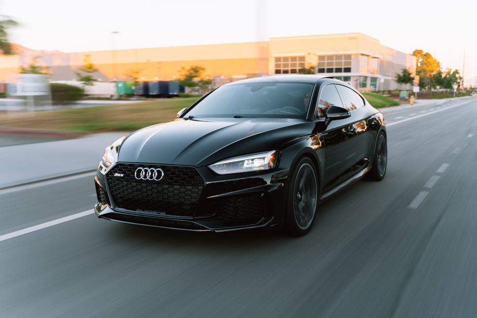 A sleek black Audi RS5 in motion on a city road during daytime.