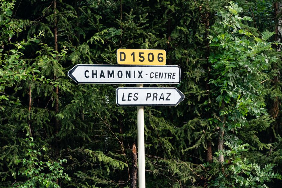 Road signs pointing to Chamonix Centre and Les Praz against a forest backdrop in France.
