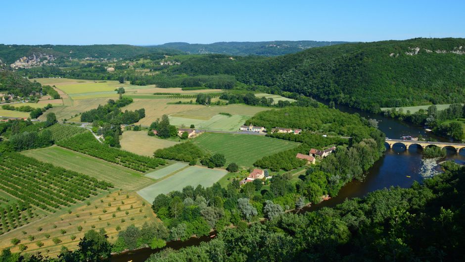 Aerial view of lush green fields, river, and a historical stone bridge in a rural setting.