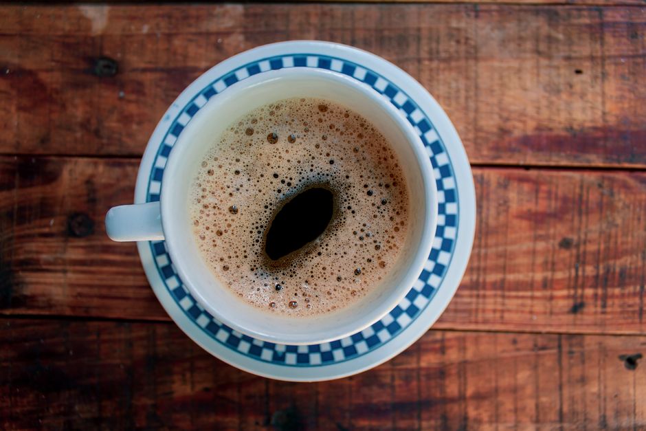 A steaming cup of coffee sits on a wooden table, offering a cozy and inviting feel.