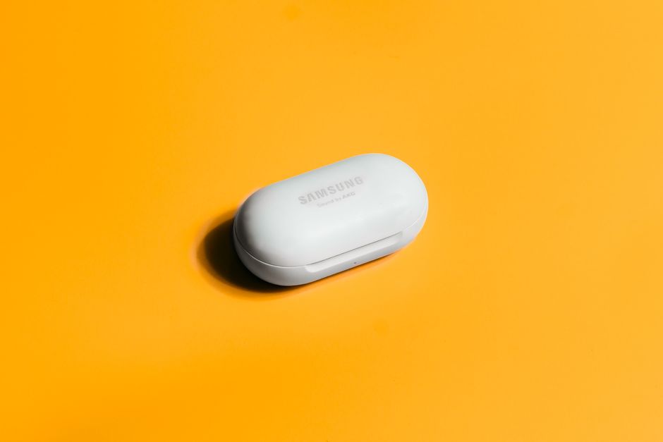 White Samsung wireless earbuds case on a bright yellow background, showcasing sleek tech design.