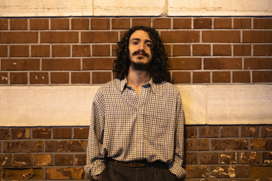 Portrait of stylish man with long hair and beard against brick wall.
