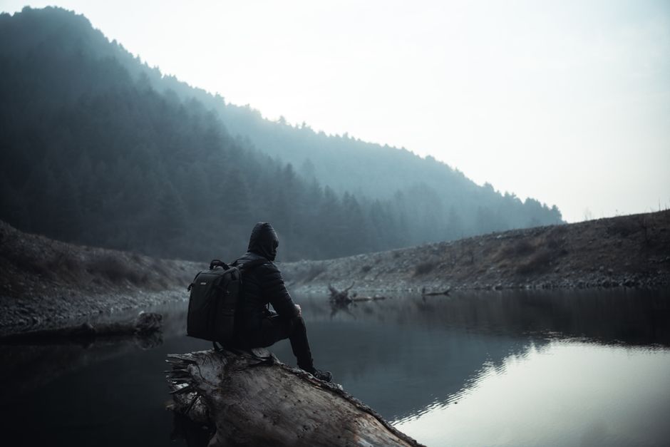 A lone hiker sits on a log by a misty mountain lake, embracing nature's tranquility.