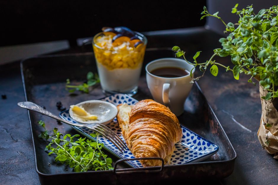 A delicious breakfast setup with a croissant, coffee, and yogurt parfait on a tray.