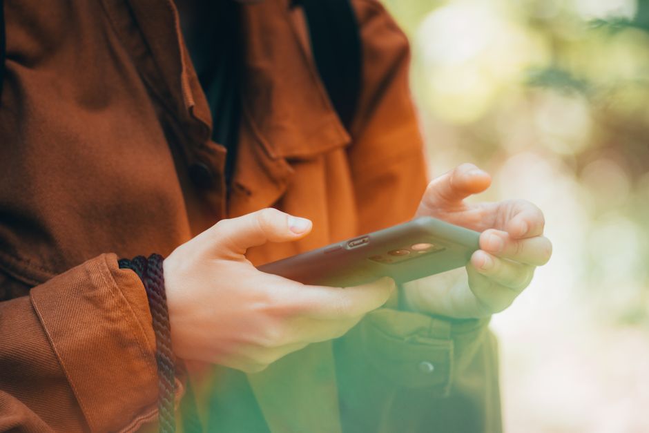 Close-up of hands using a smartphone outdoors with an autumn vibe, showcasing technology and nature.