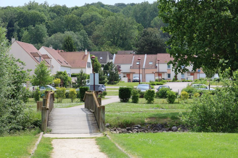 Picturesque view of a wooden footbridge leading to a peaceful village in Breuil-le-Sec, France.