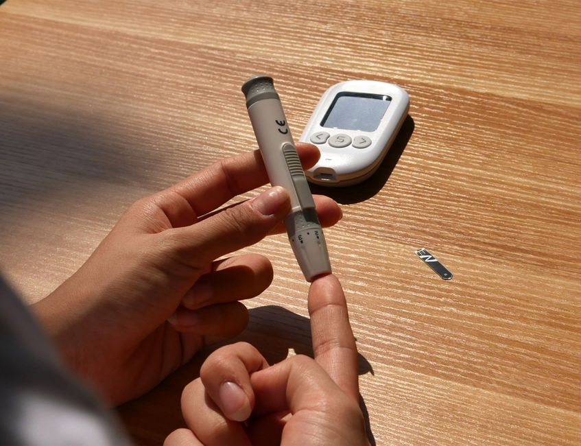 Person testing blood glucose level using blood glucose meter on wooden surface.